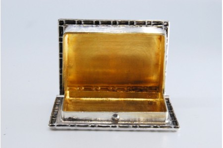 Caixa de comprimidos em prata em forma de livro com frisos gravados com interior dourado e tampa basculante.